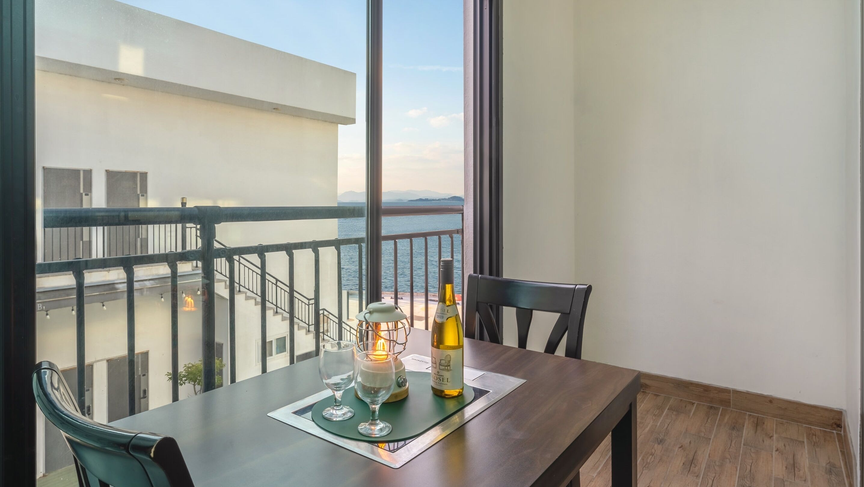 A balcony with a table set for two, a bottle of wine, and a candle.