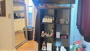 A room with a black TV stand, a mirror, and a shelf with various decorative items.
