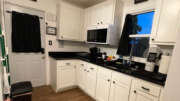 A compact kitchen with white cabinets, a microwave, a coffee maker, and a trash bin.