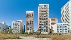 Ein Strandhotel mit mehreren Hochhäusern, einem Sandstrand und Palmen.