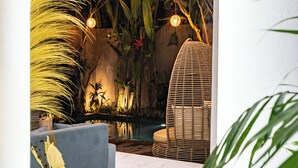 A modern interior with a marble floor, a round table with a gold base, a blue sofa, and a wicker chair. There is a small indoor garden with plants and a decorative wall. - Villa Ashëla (By JB Villas) (Bali)