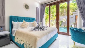 A bedroom with a large bed, a nightstand, a chair, and a view of a pool and greenery outside. - Villa Ashëla (By JB Villas) (Bali)