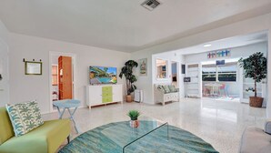 A spacious living room with a large TV, a dining area with a table and chairs, and a kitchen area with cabinets and a sink. - Tiki Lounge + Pool | 5 min to Beach & Las Olas (Fort Lauderdale)
