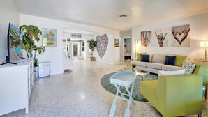 A spacious living room with a sofa, a coffee table, and a TV. There are heart-shaped decorations on the walls and a plant in the corner. - Tiki Lounge + Pool | 5 min to Beach & Las Olas (Fort Lauderdale)