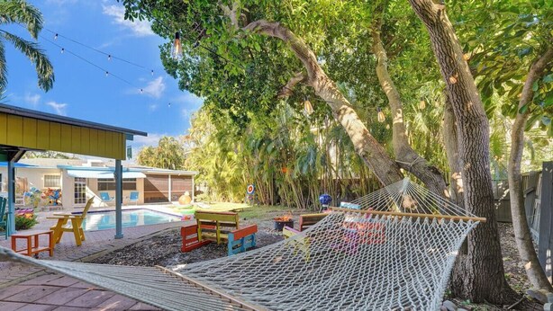 A hammock under a tree, a pool, and a building with a yellow roof. - Tiki Lounge + Pool | 5 min to Beach & Las Olas (Fort Lauderdale)
