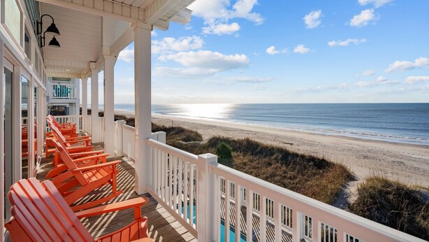 A wooden deck with orange chairs overlooking a beach. - Hailo: Spacious 7-Bedroom Oceanfront Retreat in Oak Island, NC, perfect for up to 18 guests. (Oak Island)