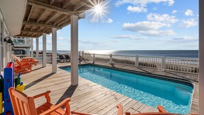 A wooden deck with a pool, lounge chairs, and a view of the ocean. - Hailo: Spacious 7-Bedroom Oceanfront Retreat in Oak Island, NC, perfect for up to 18 guests. (Oak Island)