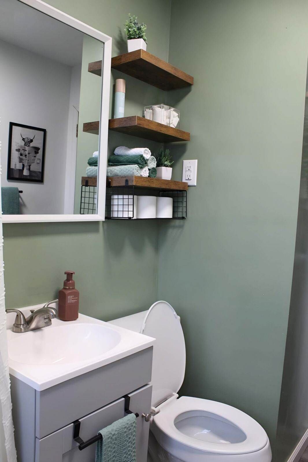 Un baño con un lavamanos blanco, un inodoro y estantes de madera sobre el inodoro que sostienen toallas y artículos de aseo.
