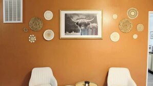 Een kamer met twee witte stoelen, een kleine ronde tafel met een kaars, en een lijst met een afbeelding van een stier aan de muur.