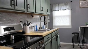 Een moderne keuken met lichtgroene kastjes, een roestvrijstalen fornuis en een houten aanrecht.