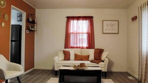 Een woonkamer met een witte bank, rode gordijnen, een zwarte salontafel en een bord met een raam op de muur.