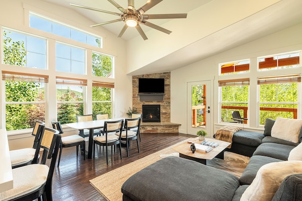 A spacious living area with a fireplace, large windows, and a ceiling fan.