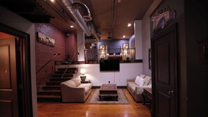 A spacious living room with a staircase, a flat-screen TV mounted on the wall, and a cozy seating area with a coffee table.
