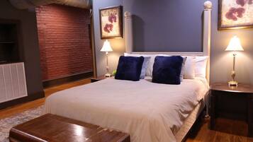 A neatly arranged bedroom with a large bed, two bedside lamps, a wooden nightstand, and a brick accent wall.