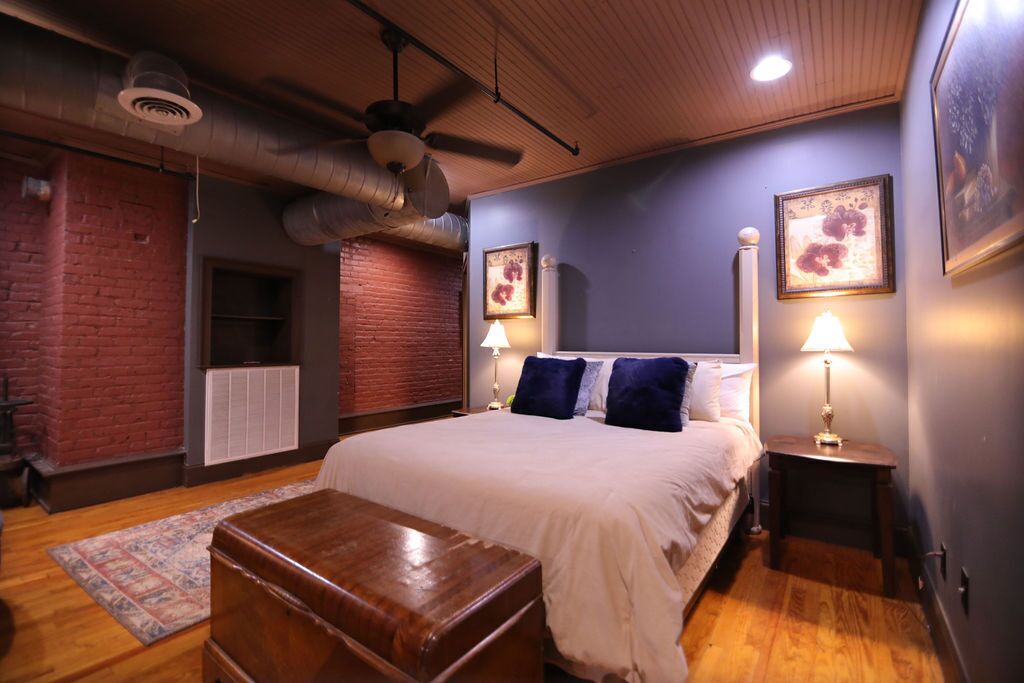Ein Schlafzimmer mit einem großen Bett, zwei Nachttischlampen, einer Holzbank, einem Heizkörper und einem Deckenventilator.