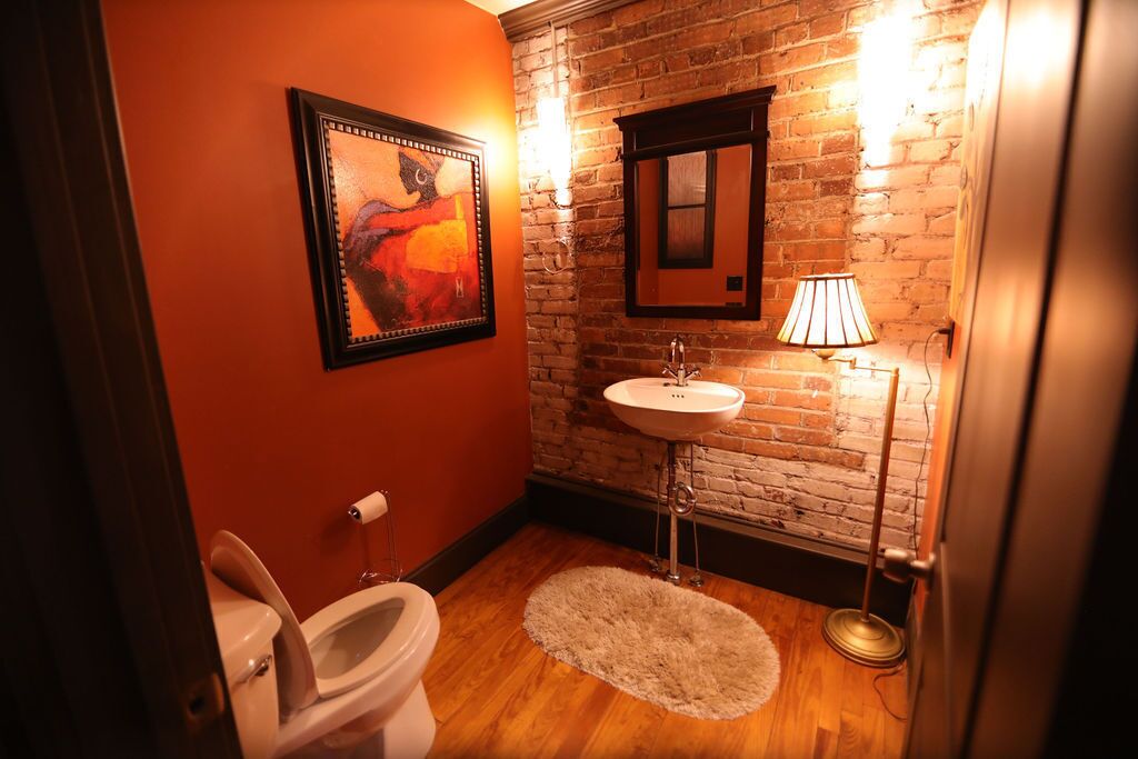 Un baño con suelo de madera, un lavabo blanco, un cuadro enmarcado y un espejo sobre el lavabo.