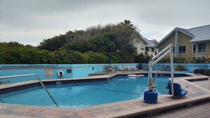 Una piscina con un cartel de prohibición de saltos, sillas de descanso y un puesto de socorrista.