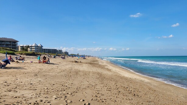 Una playa con arena, algunas personas y edificios al fondo.