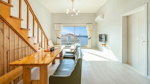 Une chambre d’hôtel moderne avec un escalier en bois, un coin repas avec un banc, un téléviseur fixé au mur et une vue sur un balcon doté d’une balustrade.