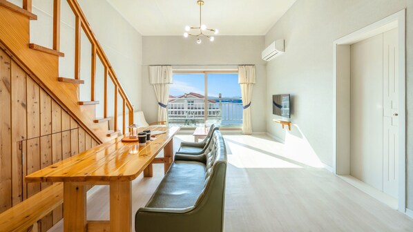 Een moderne hotelkamer met een houten trap, een zithoek met een bank, een aan de muur bevestigde televisie en uitzicht op een balkon met een hekwerk.