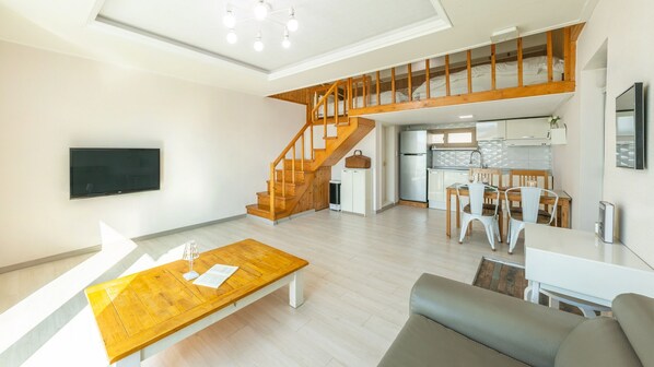 Eine moderne Wohnung mit Holztreppe, einer Küche, einem Essbereich und einem Wohnzimmer mit Fernseher und Couchtisch.