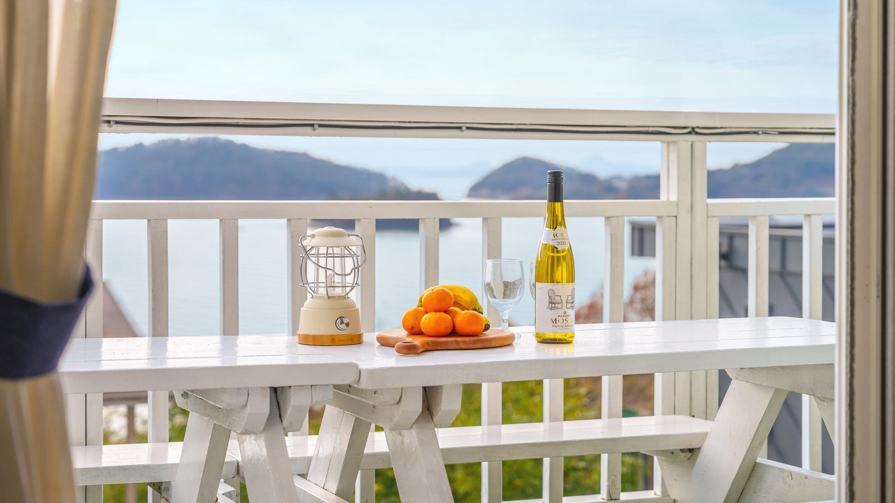 A balcony with a table set for a meal, a bottle of wine, and a lantern.