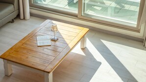 Une table basse en bois, sur laquelle sont posés un livre et une bougie, dans une pièce lumineuse dotée de grandes fenêtres.