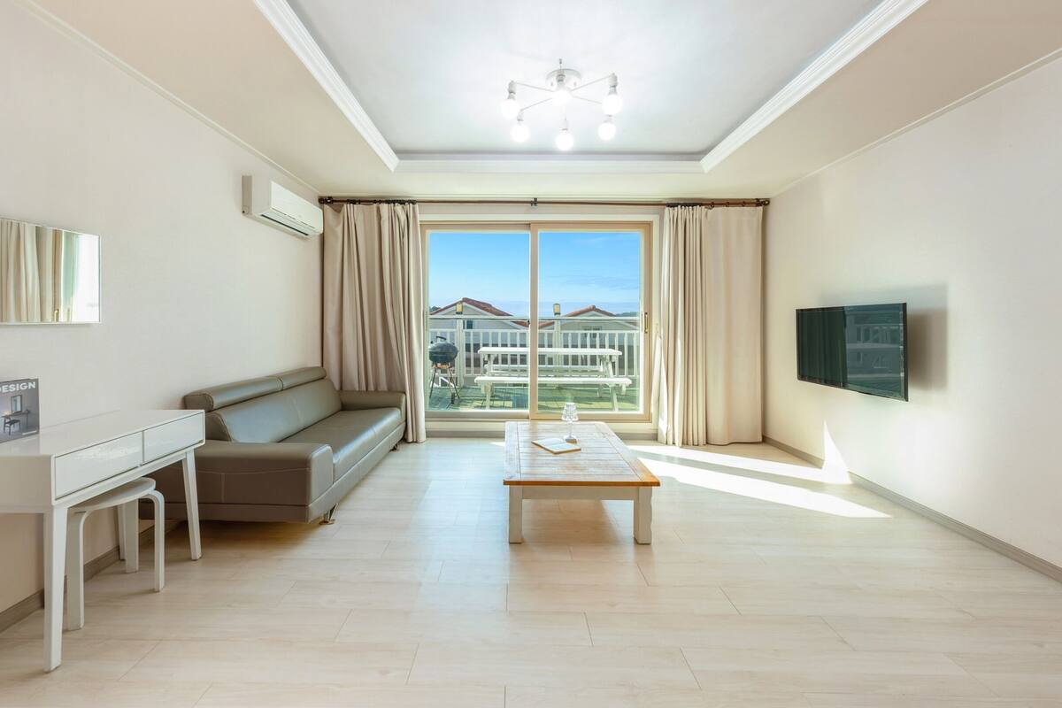 Ein modernes Wohnzimmer mit einer Couch, einem Couchtisch, einem Fernseher und einem Balkon mit Blick.