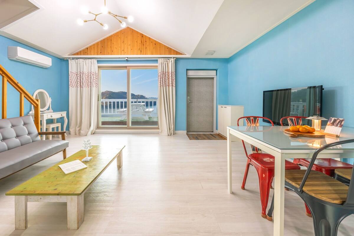 Ein modernes Wohnzimmer mit einer Couch, einem Esstisch mit Stühlen, einem Fernseher und einem Balkon mit Blick.