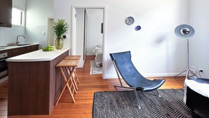 A modern kitchen with a central island, wooden flooring, a black leather chair, and a floor lamp. - Elegant Surry Hills Apartment: Steps to Cafes, City, & Sydney Icons (Darlinghurst)