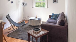 A modern living room with a ceiling fan, a window with a view, a black leather chair, a brown sofa, and a small round table. - Elegant Surry Hills Apartment: Steps to Cafes, City, & Sydney Icons (Darlinghurst)