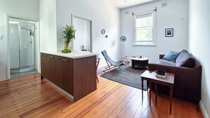 A modern living space with a kitchen island, a seating area with a sofa and a chair, a small table, and a floor lamp. - Elegant Surry Hills Apartment: Steps to Cafes, City, & Sydney Icons (Darlinghurst)
