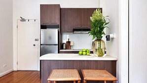 A modern kitchen with dark wood cabinets, a stainless steel refrigerator, a white countertop, and a vase with green plants. - Elegant Surry Hills Apartment: Steps to Cafes, City, & Sydney Icons (Darlinghurst)