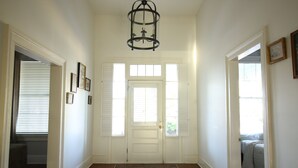 Ein Flur mit einem gemusterten Teppich, einer weißen Tür mit Fensterläden und einem Chandelier.