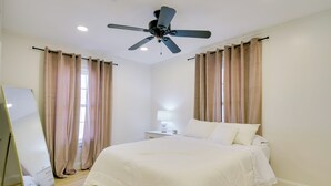 Une chambre à coucher avec un lit, un ventilateur de plafond, une table de chevet avec une lampe et un miroir.