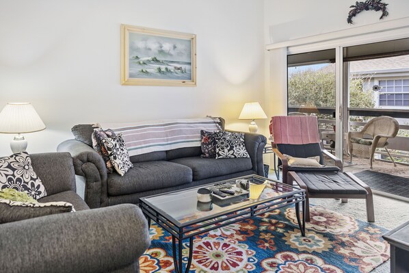 A living room with a sofa, armchairs, a coffee table, and a balcony with outdoor furniture. - 273 Sea Woods Veranda 3BD - Keep Palm & Carry On (New Smyrna Beach)
