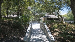 A wooden bridge leading to a building surrounded by trees. - 273 Sea Woods Veranda 3BD - Keep Palm & Carry On (New Smyrna Beach)