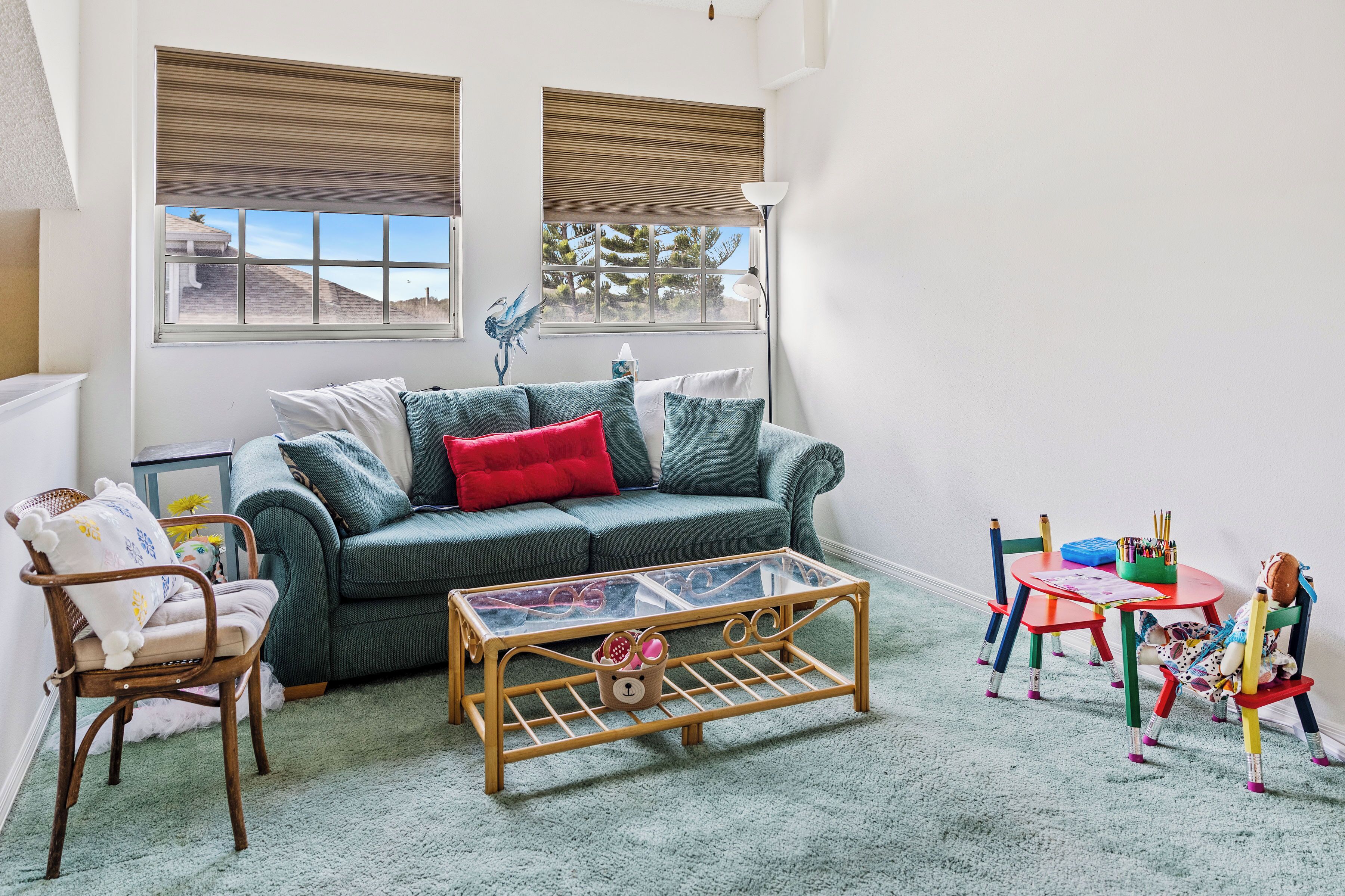 A cozy living room with a green sofa, a glass coffee table, and a small table with toys and a lamp.