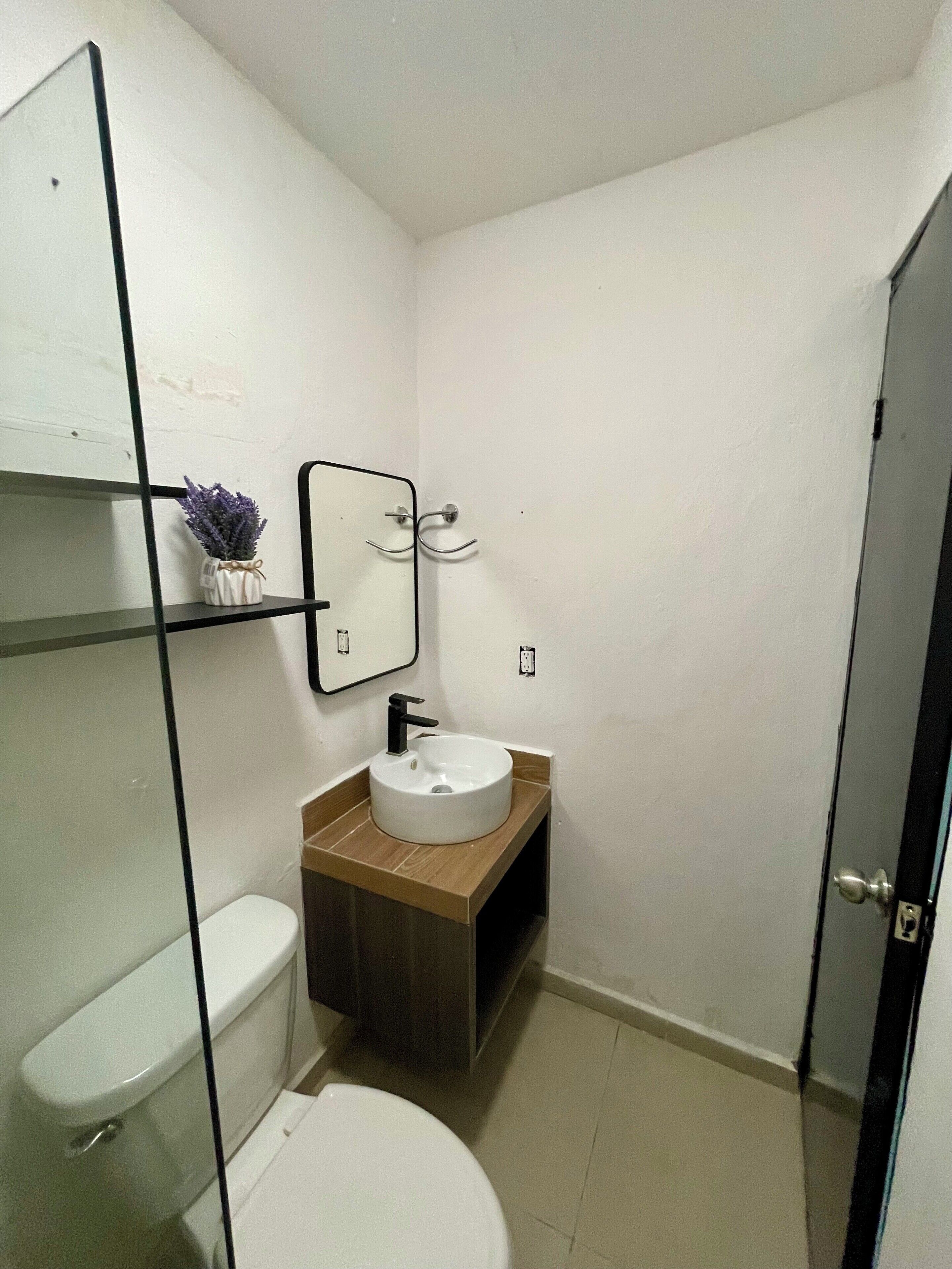 Et lille badeværelse med toilet i hvidt, hvid vask med træbordplade, og et spejl over vasken.