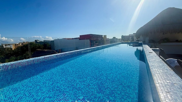 A swimming pool with blue tiled flooring, surrounded by buildings and a clear sky. - Coco Azul Hotel Boutique (Playa del Carmen)