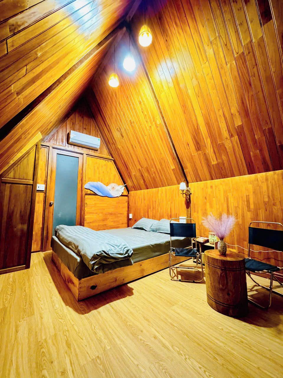 A cozy attic bedroom with a sloped ceiling, wooden walls, a bed, a chair, and a small table with a vase.