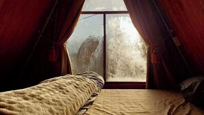 Une chambre confortable située dans les combles, avec une grande fenêtre, des poutres apparentes et un lit recouvert d’une couverture matelassée.