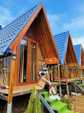 Une cabane en bois avec un toit en pente, une fenêtre visible et un petit espace extérieur aménagé pour s’asseoir.
