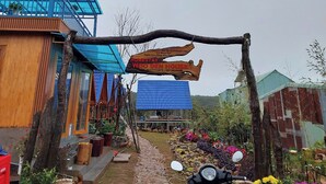 Une maison de campagne au toit bleu, avec une véranda en bois et une enseigne.