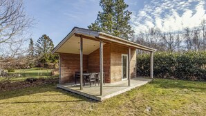 Een houten vakantiehuisje met een overdekt terras, een eettafel en stoelen.