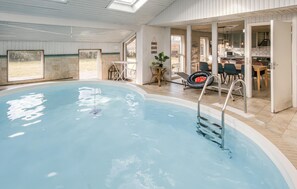 An indoor swimming pool with a clear view of the adjacent kitchen area, a dining table, and a chair.