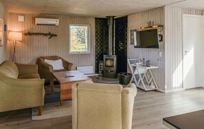 A cozy room with wooden walls, a fireplace, a TV mounted on the wall, and a small table with chairs.