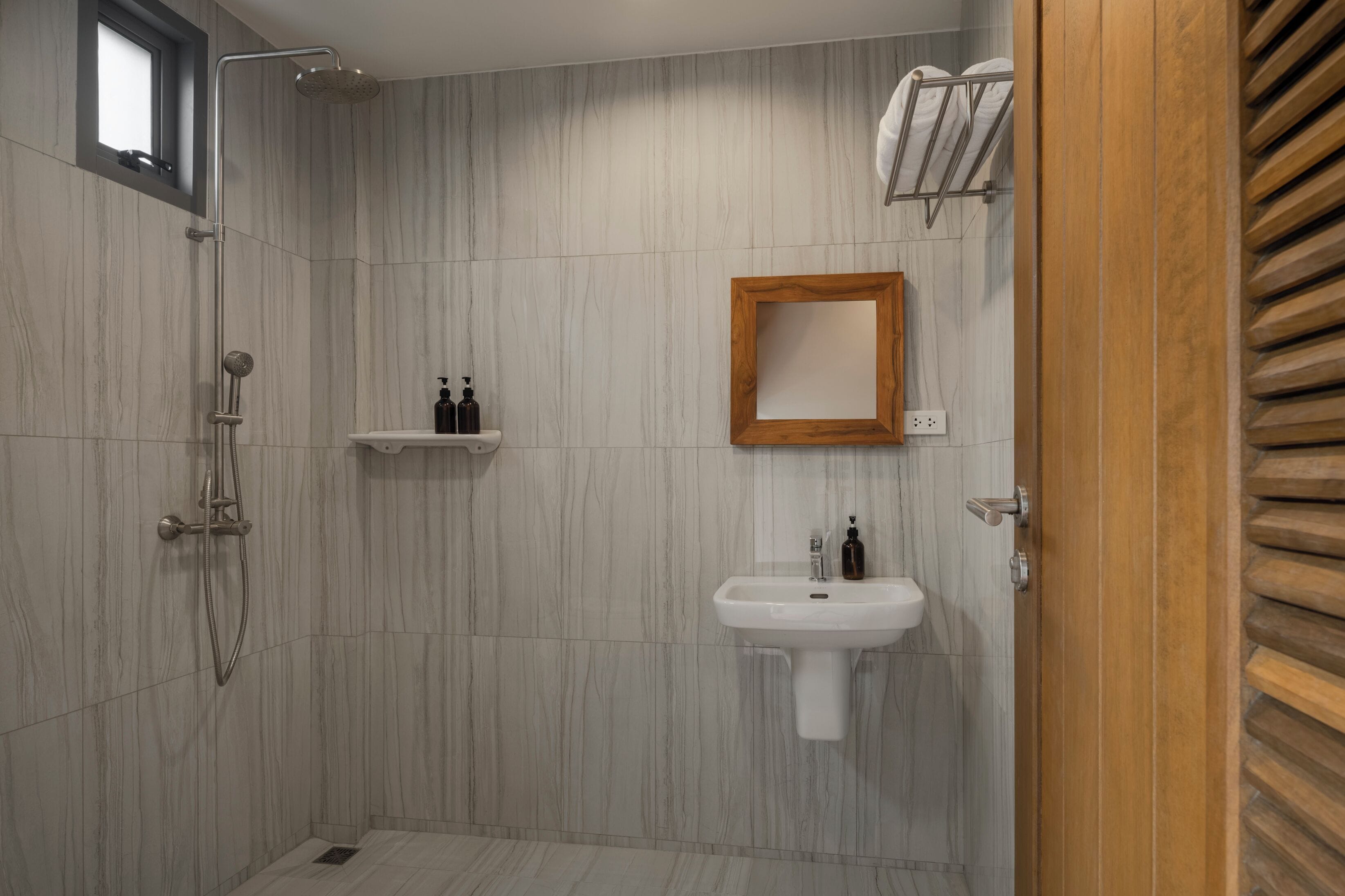 A modern bathroom with a shower, sink, and wooden vanity.