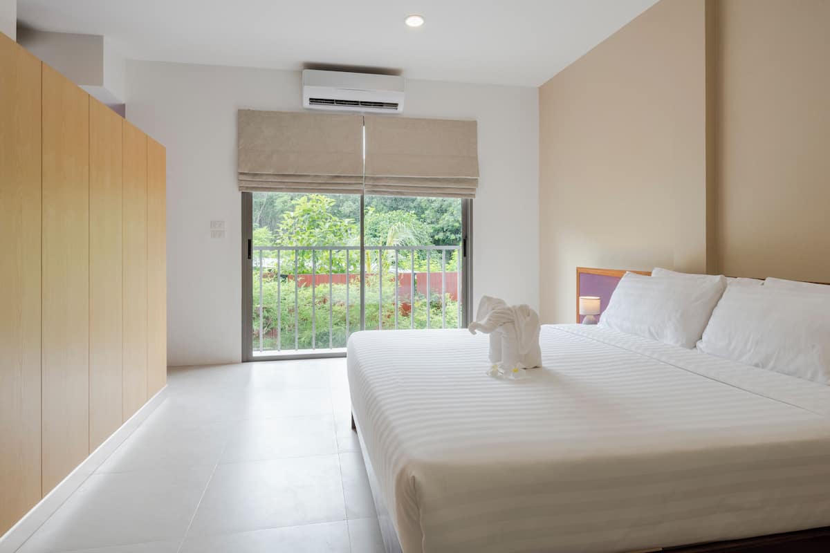 A modern hotel room with a large bed, a wooden wardrobe, and a view of greenery outside.