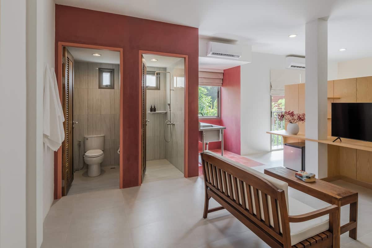 A modern bathroom with a shower, toilet, and vanity. There is a wooden bench and a TV mounted on the wall.